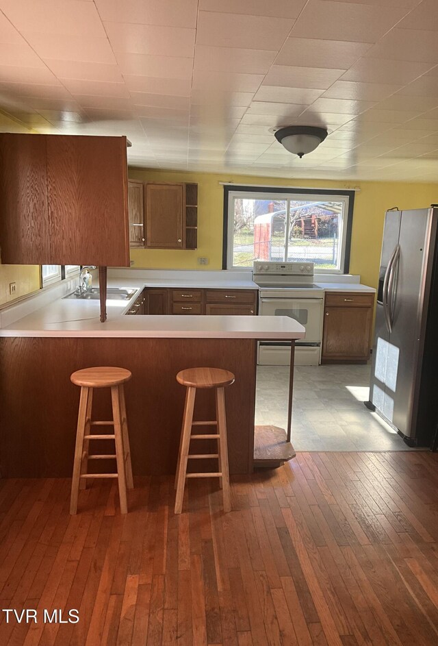 kitchen with white range with electric stovetop, a sink, a peninsula, stainless steel fridge with ice dispenser, and hardwood / wood-style flooring