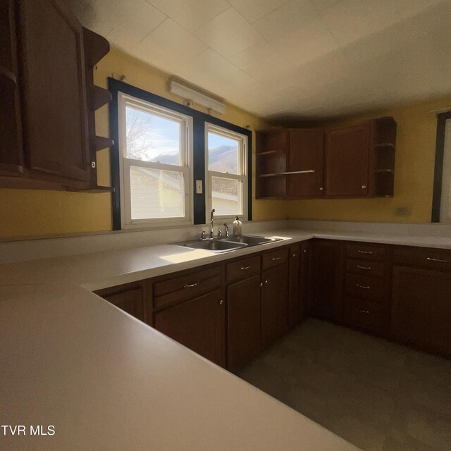 kitchen with light countertops, a sink, dark brown cabinetry, and open shelves