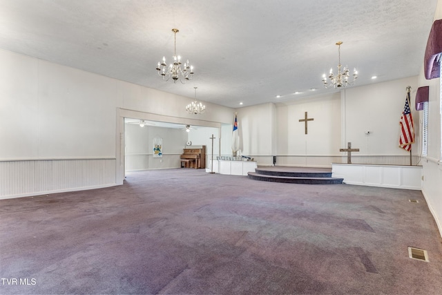 carpeted spare room featuring ceiling fan with notable chandelier and a textured ceiling