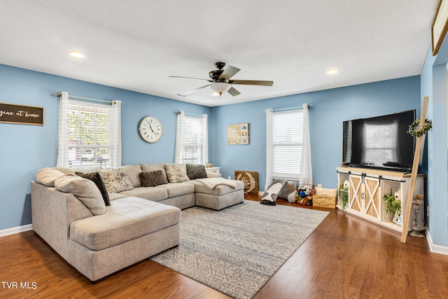 living room featuring dark hardwood / wood-style flooring, ceiling fan, and a textured ceiling