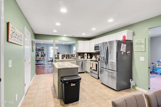 kitchen featuring stainless steel appliances, light stone counters, light tile patterned flooring, a center island, and white cabinetry
