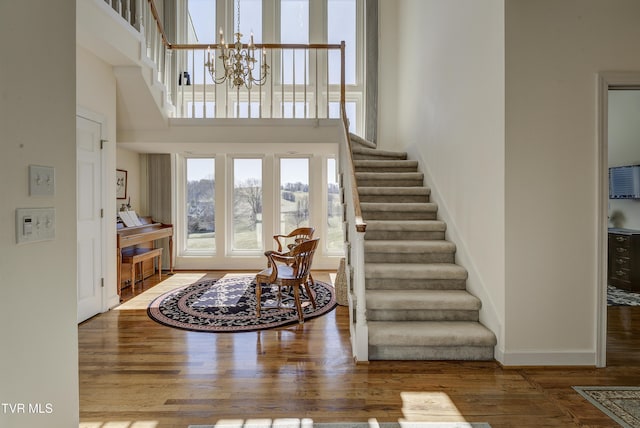 foyer entrance with baseboards, a towering ceiling, wood finished floors, an inviting chandelier, and stairs