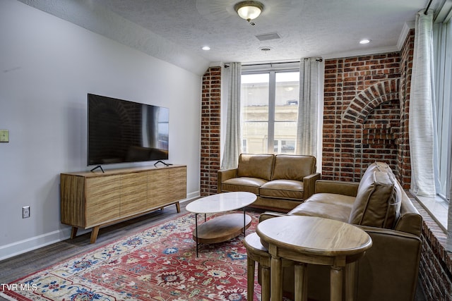 living area featuring brick wall, baseboards, a textured ceiling, and wood finished floors