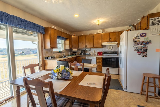 kitchen featuring white appliances, brown cabinets, light countertops, under cabinet range hood, and a sink