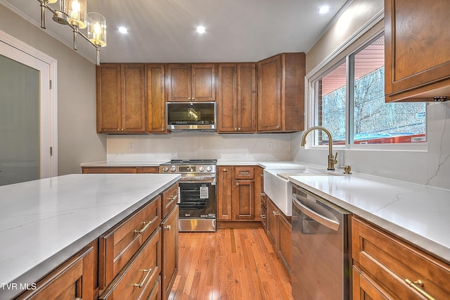 kitchen with pendant lighting, brown cabinets, light wood finished floors, appliances with stainless steel finishes, and a sink