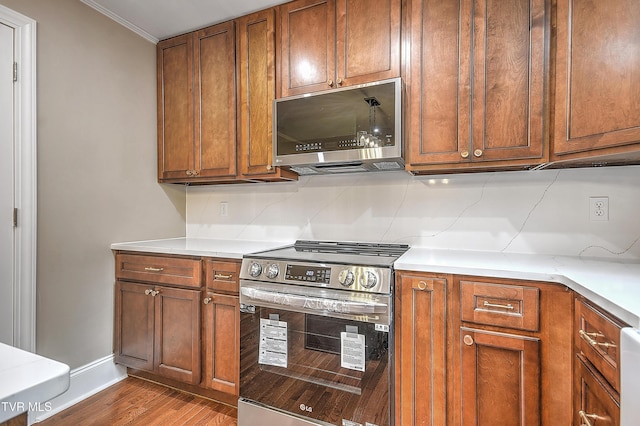 kitchen with brown cabinets, appliances with stainless steel finishes, light countertops, and wood finished floors