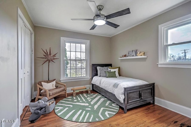 bedroom featuring baseboards, a ceiling fan, ornamental molding, wood finished floors, and a closet