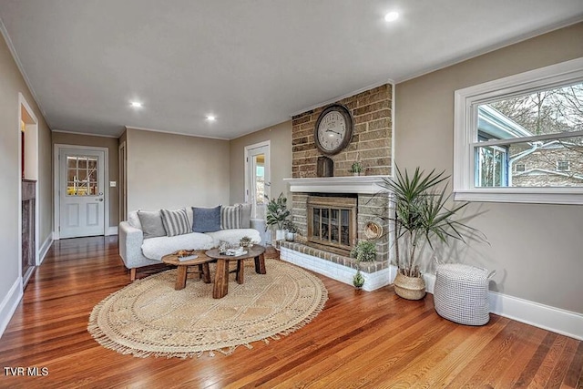 living area with plenty of natural light, a brick fireplace, wood finished floors, and baseboards