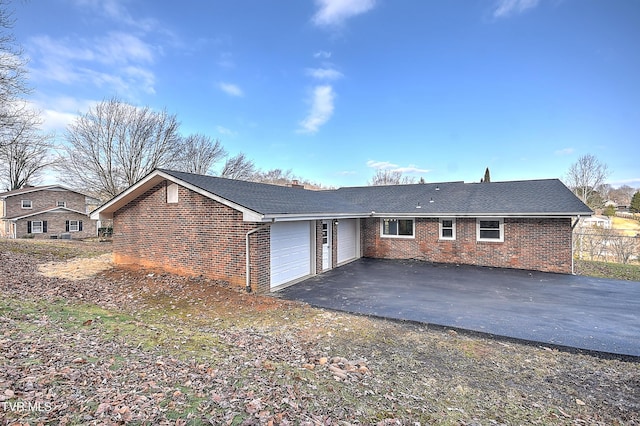 rear view of house featuring a garage, driveway, brick siding, and a chimney