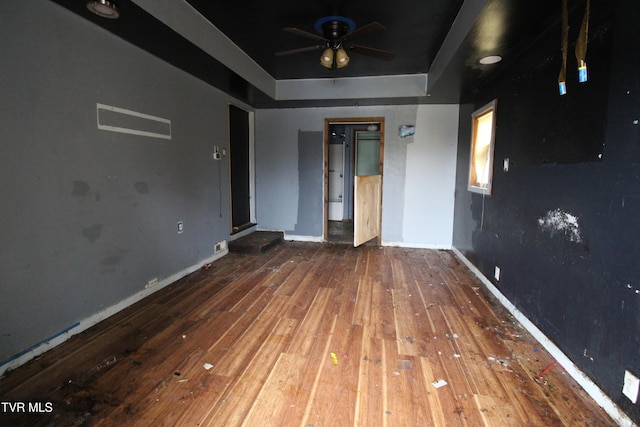 empty room with hardwood / wood-style flooring, ceiling fan, and a raised ceiling