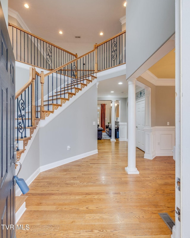 entryway with crown molding, light wood-style floors, and ornate columns