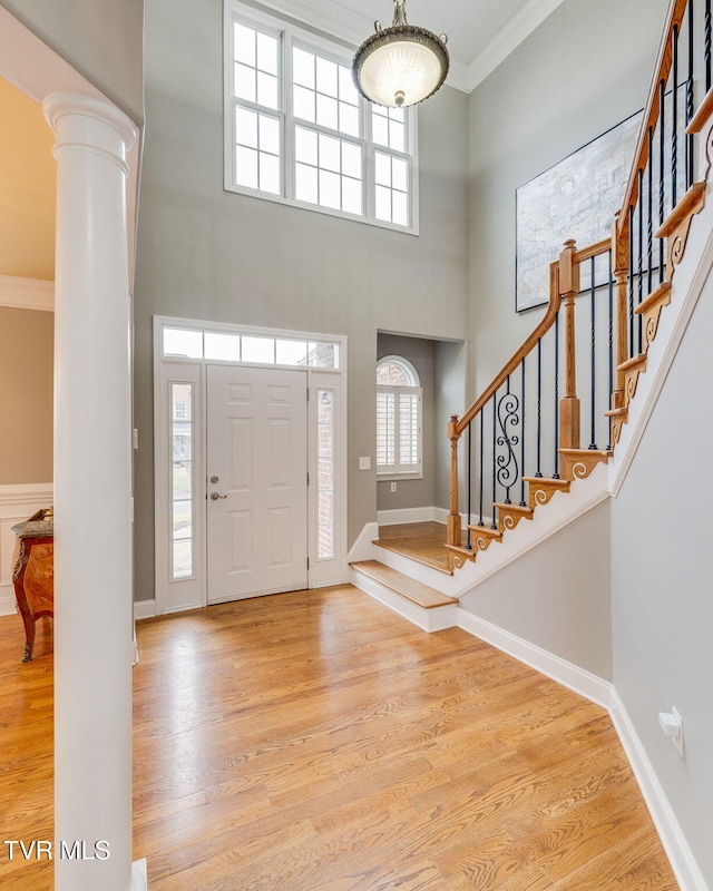 foyer with light wood finished floors, baseboards, stairs, crown molding, and ornate columns