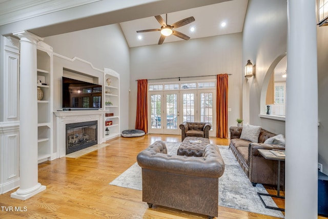 living area featuring a ceiling fan, a towering ceiling, a premium fireplace, light wood-type flooring, and ornate columns