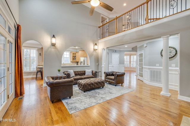 living area featuring a ceiling fan, light wood-type flooring, visible vents, and ornate columns