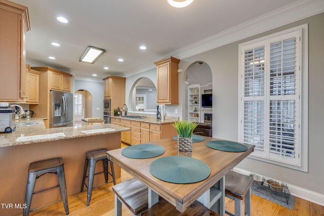 kitchen featuring arched walkways, light brown cabinets, a peninsula, a sink, and appliances with stainless steel finishes