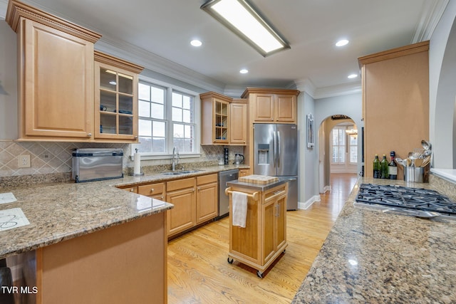 kitchen with light brown cabinets, arched walkways, stainless steel appliances, and a sink