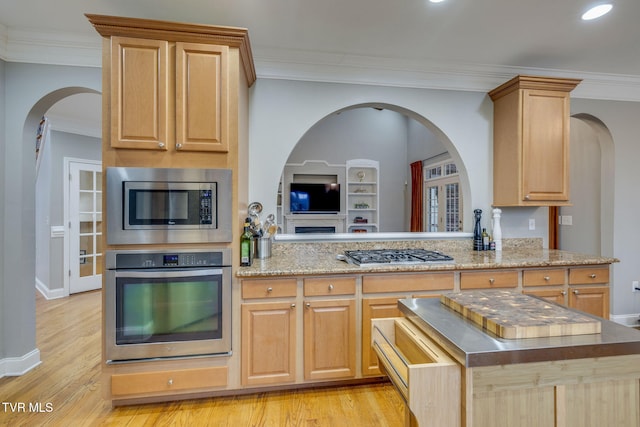 kitchen with light brown cabinets, a peninsula, appliances with stainless steel finishes, light wood-type flooring, and crown molding