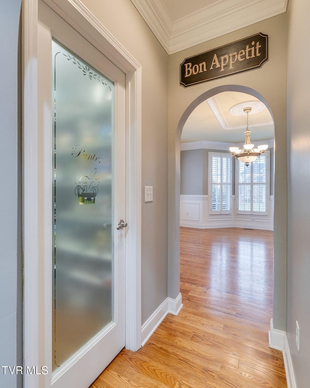 hall with arched walkways, light wood finished floors, a decorative wall, and crown molding