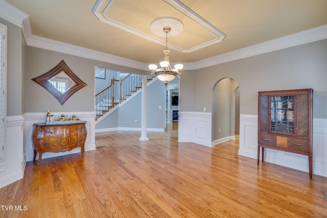 interior space with wainscoting, stairway, ornamental molding, light wood-style floors, and a notable chandelier