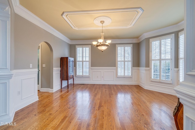 spare room with arched walkways, a notable chandelier, light wood-style floors, wainscoting, and crown molding