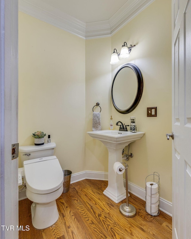 half bath with toilet, crown molding, baseboards, and wood finished floors