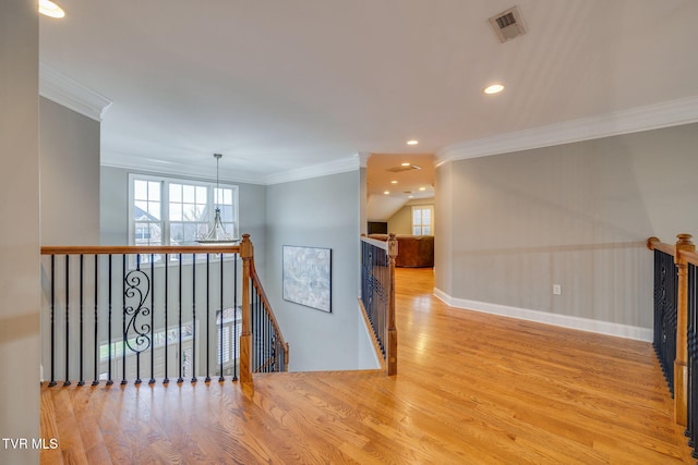 hall with light wood finished floors, visible vents, crown molding, and an upstairs landing