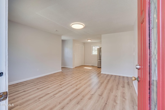 unfurnished room featuring light wood-style flooring, baseboards, and a textured ceiling