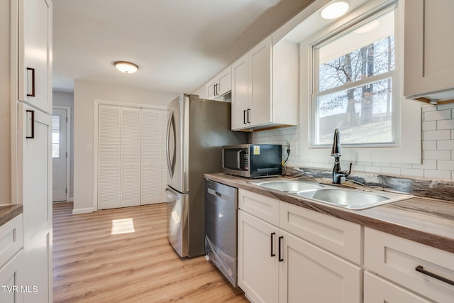 kitchen featuring light wood-type flooring, appliances with stainless steel finishes, decorative backsplash, and a sink