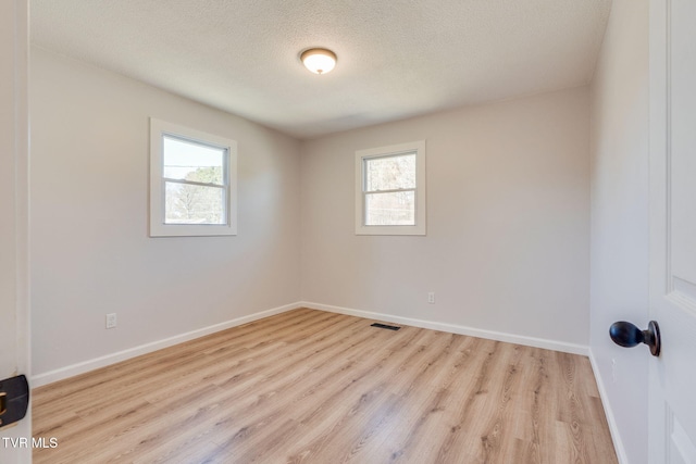 unfurnished room featuring light wood-style flooring, plenty of natural light, a textured ceiling, and baseboards