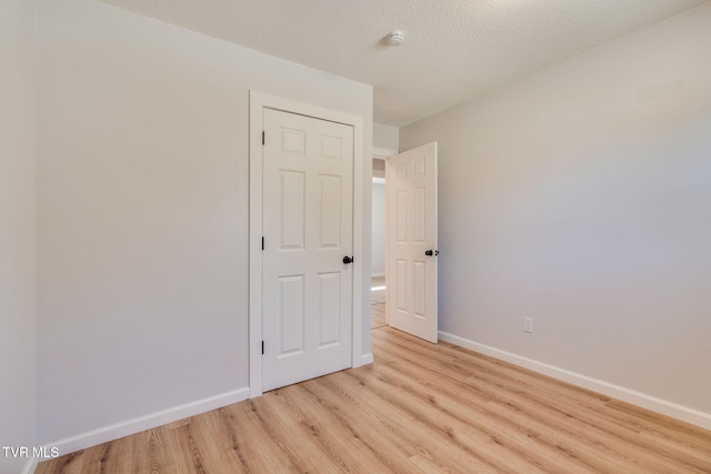 unfurnished bedroom with light wood-type flooring, a textured ceiling, and baseboards