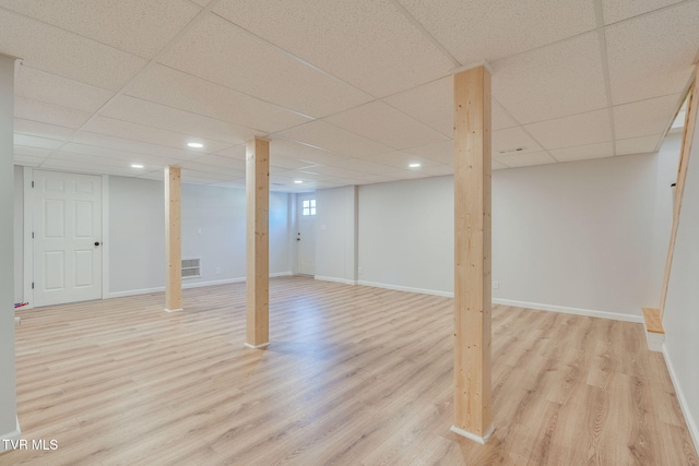 finished below grade area featuring a paneled ceiling, light wood finished floors, and baseboards