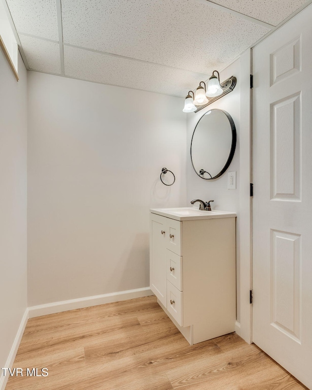 bathroom with a paneled ceiling, baseboards, wood finished floors, and vanity