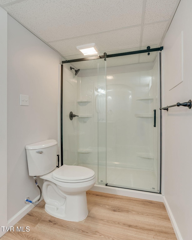 bathroom featuring toilet, a stall shower, wood finished floors, a drop ceiling, and baseboards