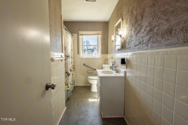 bathroom with visible vents, toilet, a wainscoted wall, vanity, and tile walls