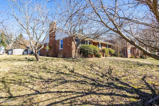 view of side of home featuring a yard, a chimney, and brick siding