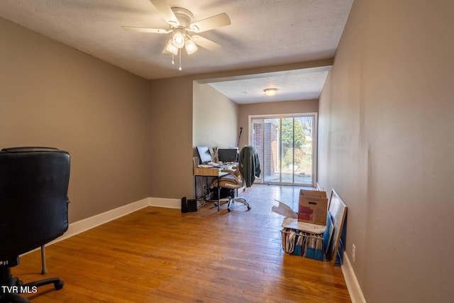 office space featuring baseboards, a textured ceiling, a ceiling fan, and light wood-style floors