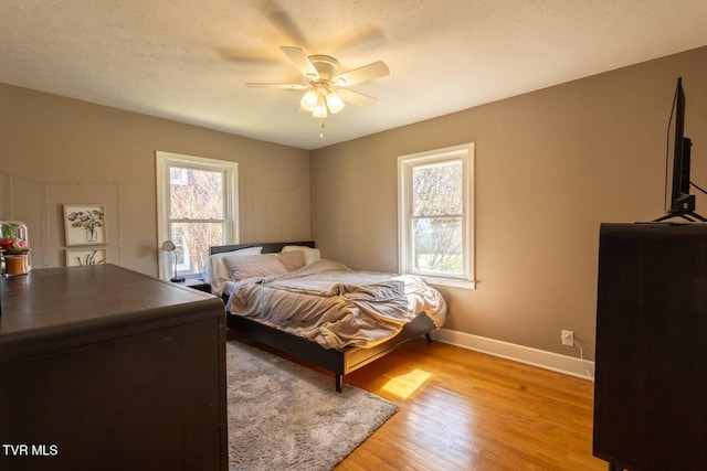 bedroom featuring a textured ceiling, light wood finished floors, a ceiling fan, and baseboards