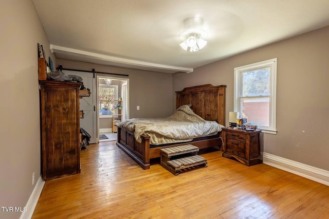 bedroom featuring light wood finished floors, a barn door, and multiple windows