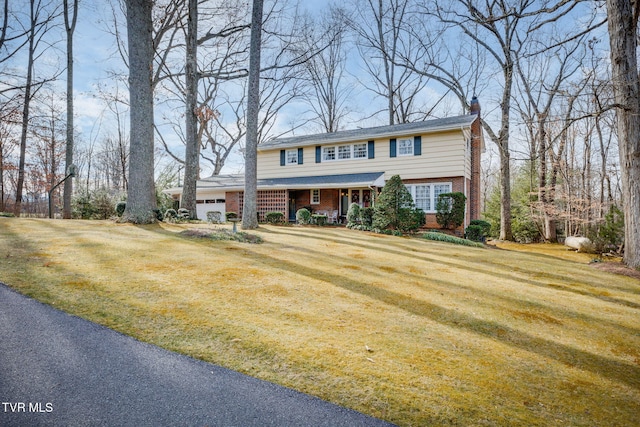 colonial home featuring a garage, brick siding, driveway, a front lawn, and a chimney