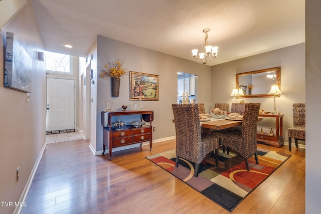 dining space featuring a chandelier, a textured ceiling, baseboards, and wood finished floors