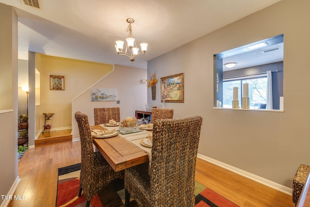 dining room featuring a chandelier, baseboards, visible vents, and light wood finished floors