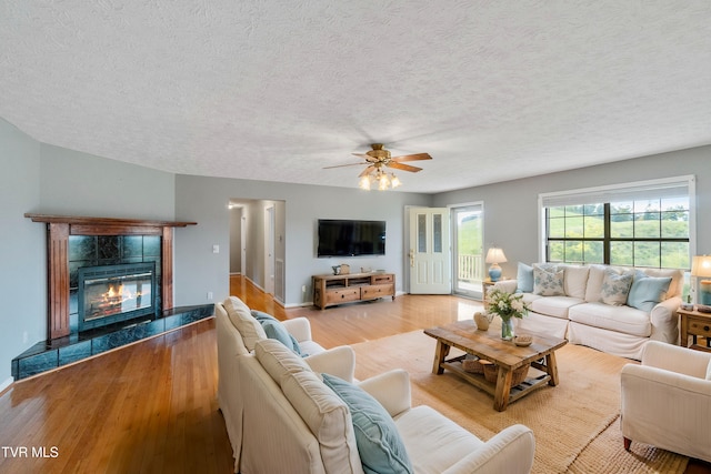 living room with light hardwood / wood-style floors, a tiled fireplace, ceiling fan, and a textured ceiling