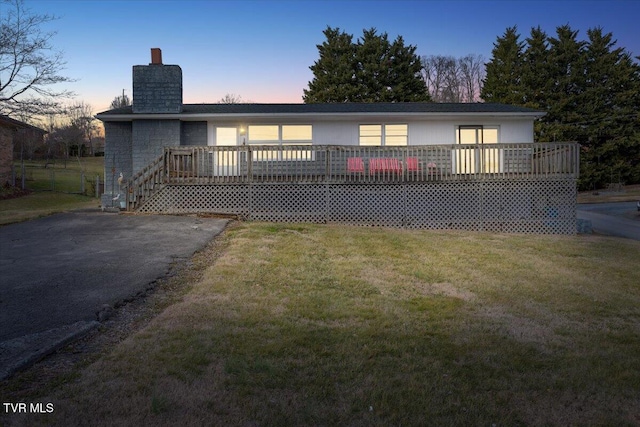 back of property featuring a lawn, a chimney, and a wooden deck