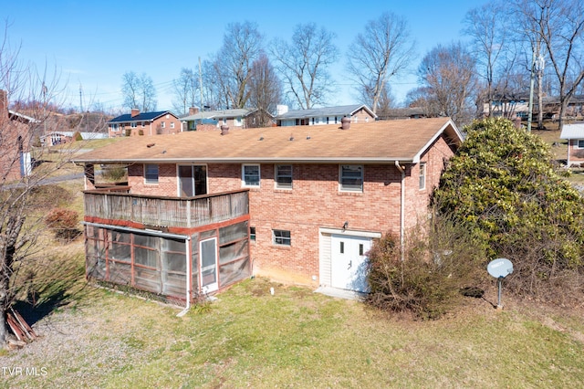 rear view of property featuring brick siding, a sunroom, a residential view, and a lawn