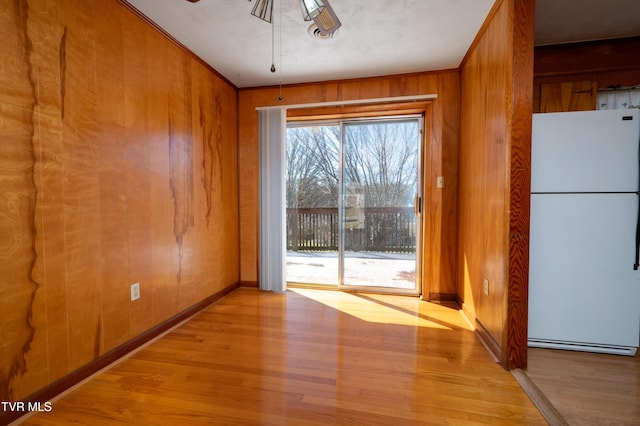 unfurnished dining area with light wood finished floors, crown molding, and wood walls