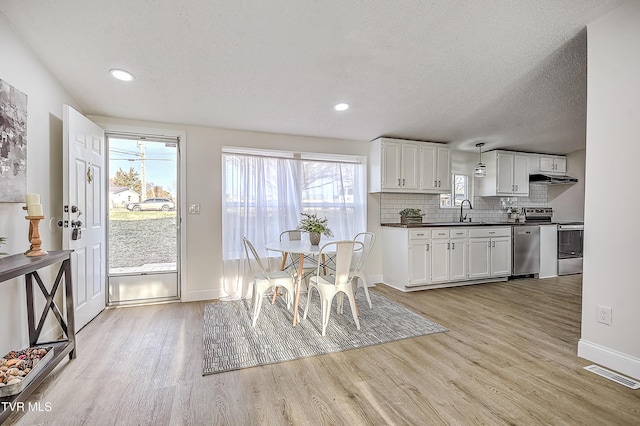 kitchen with white cabinets, sink, stainless steel appliances, and decorative light fixtures