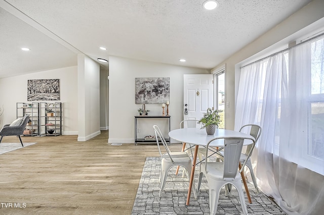 dining area with light wood-type flooring, lofted ceiling, a wealth of natural light, and a textured ceiling