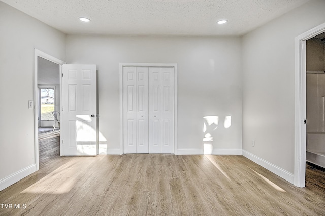 unfurnished bedroom with light hardwood / wood-style flooring, a textured ceiling, and a closet