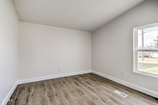 unfurnished room featuring light hardwood / wood-style floors, vaulted ceiling, and a textured ceiling