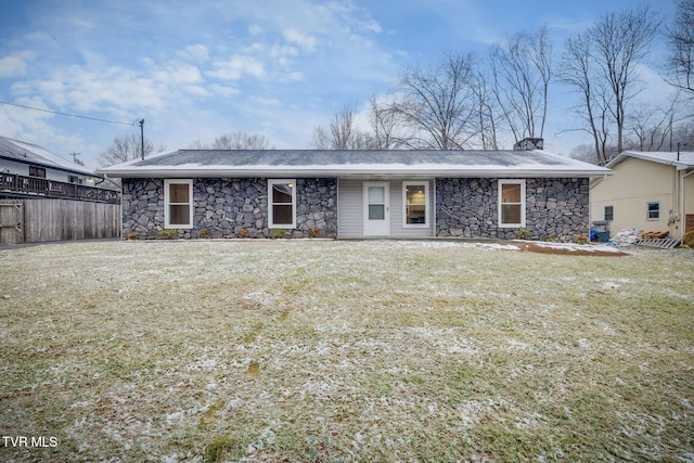 back of property featuring stone siding, a lawn, and fence